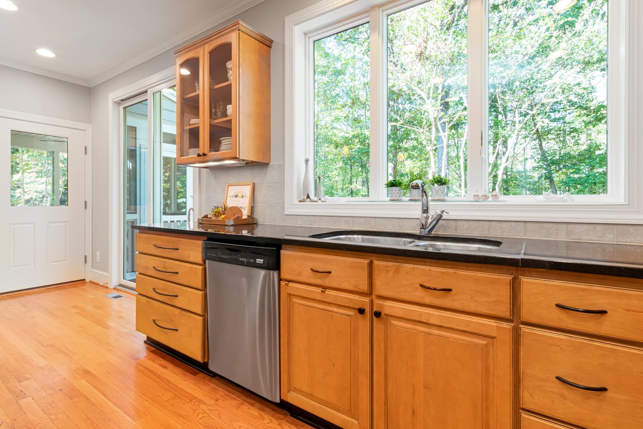 Spacious kitchen featuring wooden cabinets, large windows, and a stainless steel dishwasher.