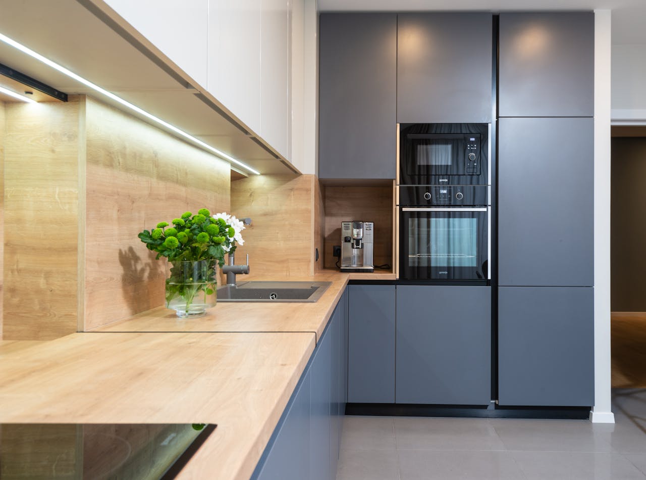 Creative design of kitchen with flowers in vase on table against coffeemaker and oven built in cupboard at home